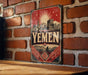 a vintage-style sign with the word "YEMEN" prominently displayed, hanging on a brick wall.