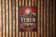 A vintage-style poster with the word "YEMEN" prominently displayed, featuring a cityscape and a sunburst design.