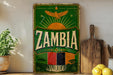 a vintage-style sign for Zambia, with a green background and a yellow eagle. The sign is placed on a shelf next to a wooden cutting board and some lemons.