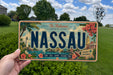 A person is holding a license plate that says "NASSAU" in bold letters, with a tropical island scene on the background.