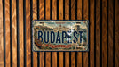 A vintage-style license plate from Hungary that says "BUDAPEST" and features an illustration of the city of Budapest.