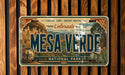 A vintage-style license plate for the Mesa Verde National Park in Colorado, featuring an illustration of the iconic mesa and surrounding landscape.