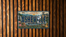 A vintage license plate from North Carolina, featuring the city of Asheville, is displayed against a wooden background.