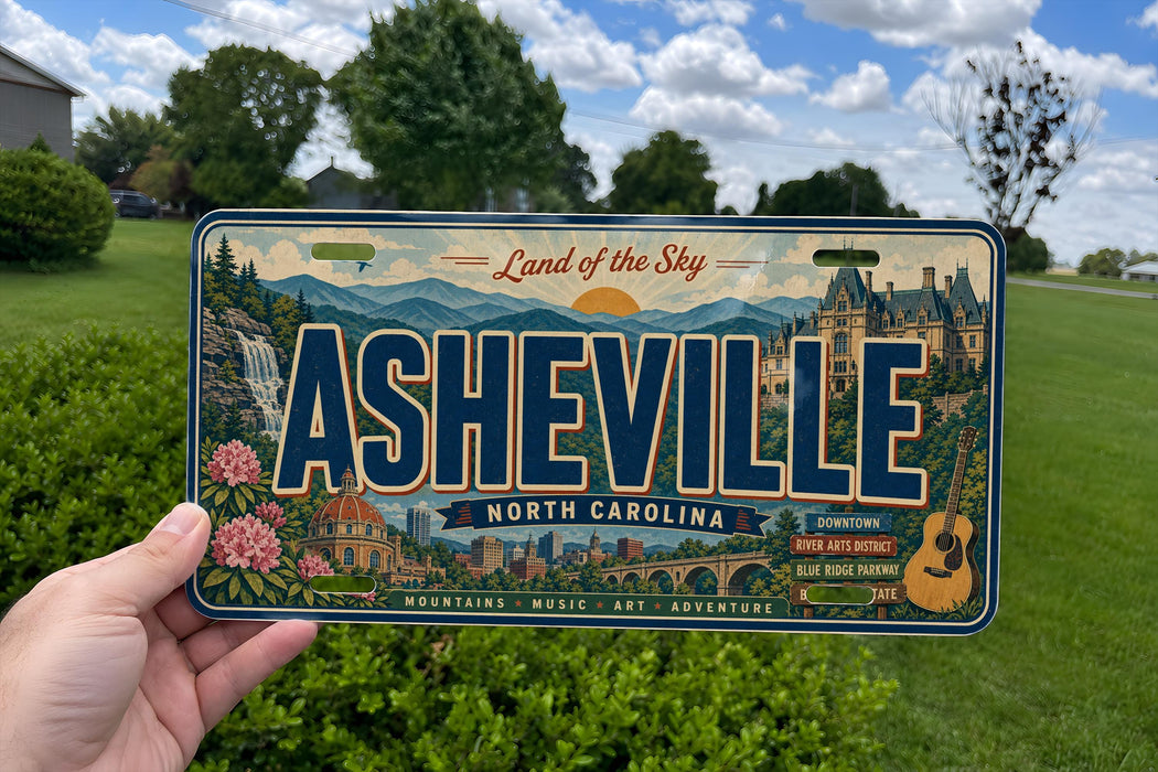 A person is holding a license plate with the text "Land of the Sky" and "Ahesville North Carolina" on it, with a scenic background of mountains, buildings, and a blue sky.