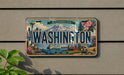 A vintage Washington state license plate with a scenic mountain backdrop and various landmarks, including a lighthouse and a ship, is displayed on a wall.