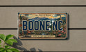 A vintage-style license plate with the text "BOONE, NC" and a scenic mountain landscape.