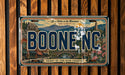 A vintage license plate from Boone, North Carolina, with a scenic mountain landscape and buildings in the background.