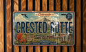 A vintage license plate from Colorado, featuring the name "Crested Butte" and a scenic mountain landscape.