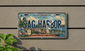 A vintage license plate from New York, with the text "Sag Harbor" prominently displayed. The plate also features a lighthouse, a sailboat, and other nautical elements, suggesting it is a souvenir or decorative item.