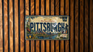 A vintage Pittsburgh license plate is displayed on a wooden wall.