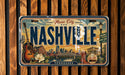 A vintage-style license plate from Tennessee, featuring the text "Music City" and "Nashville" along with various cityscape elements such as a bridge, a guitar, and a flower.