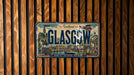 A vintage license plate from Scotland, featuring the city of Glasgow, is displayed on a wooden wall.
