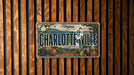 A vintage Virginia license plate with the text "CHARLOTTE'SVILLE" and "FOUNDED 1792" displayed on a wooden background.
