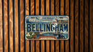 A vintage license plate from Washington, called the "Bellingham" license plate, is displayed on a wooden wall.