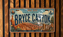 A vintage license plate with a scenic illustration of Bryce Canyon National Park, featuring mountains, canyons, and various natural elements.