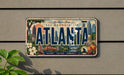 A license plate with the text "ATLANTA" and various cityscape elements, including a ferris wheel, buildings, and a bridge, mounted on a wall.