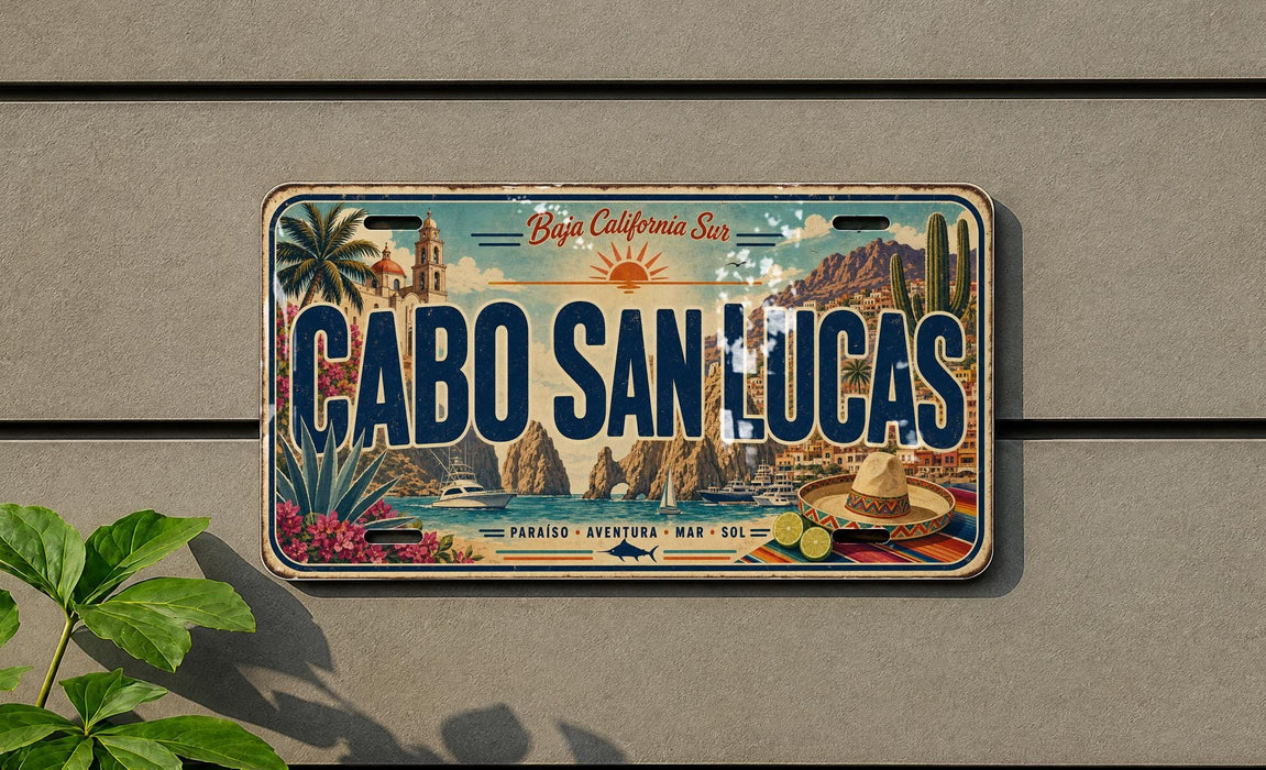A vintage license plate with the text "CABO SAN LUCAS" printed on it, featuring a scenic illustration of a coastal town with palm trees, mountains, and a sunny sky.