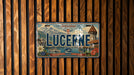 A vintage license plate from Switzerland with the word "LUCERNE" prominently displayed, featuring a scenic mountain landscape and a castle.