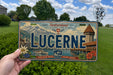 A person is holding a Swiss license plate with the word "LUCERNE" prominently displayed on it.