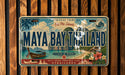 A vintage-style license plate from the island of Maya Bay, Thailand, featuring a tropical landscape with palm trees, a boat, and other scenic elements.