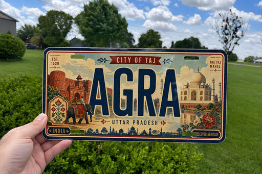A person is holding a license plate that says "AGRA" with the city of Taj Mahal in the background.