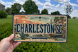 A person is holding a license plate with the text "CHARLESTON SC" on it, which is a historic charm of Lowcountry South Carolina.