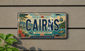 A license plate from Australia, with the word "CAIRNS" prominently displayed, is mounted on a wall.