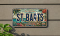 A vintage license plate from St. Bart's Island, featuring a tropical landscape with palm trees, flowers, and a body of water.