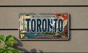 A vintage license plate from Toronto, Canada, featuring a colorful illustration of the city skyline and water.