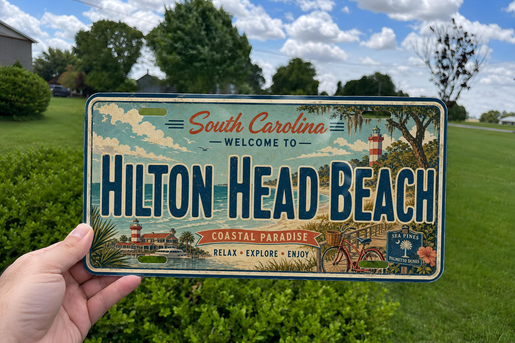 A person is holding a license plate that says "South Carolina Welcome to Hilton Head Beach" with a coastal theme featuring a lighthouse, palm trees, and a bicycle.