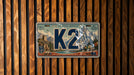 A vintage-style license plate with a mountain landscape design, mounted on a wooden wall.