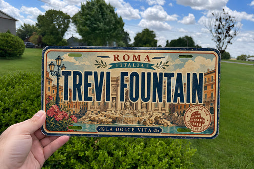 A person is holding a license plate that says "Roma Italy Trevi Fountain" with a cityscape and fountain image on it.