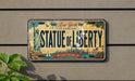 A vintage New York license plate with the text "STATUE OF LIBERTY" and the phrase "LADY LIBERTY WELCOMES YOU" printed on it.