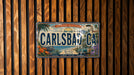 A vintage license plate from California, featuring a beach scene and a car, is displayed on a wooden wall.