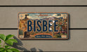 A vintage Arizona license plate with the word " Bisbee" prominently displayed, featuring a colorful illustration of a desert landscape with mountains in the background.