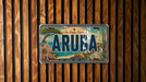 A vintage license plate from Aruba, featuring a tropical island landscape with palm trees, a lighthouse, and a beach.