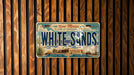 A vintage license plate from New Mexico, with the text "New Mexico" and "Land of Enchantment" printed on it, along with the word "WHITE SAND" prominently displayed.