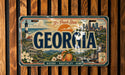A vintage Georgia license plate with a scenic illustration of the state's landmarks and natural beauty.