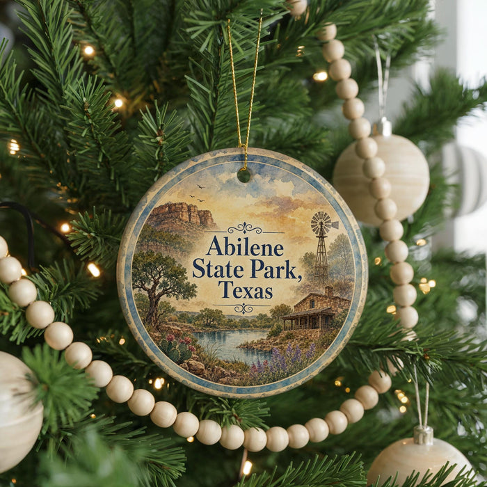 A round ornament hanging on a Christmas tree, featuring a scenic landscape with a windmill and a river.