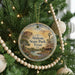 A round ornament hanging on a Christmas tree, featuring a scenic landscape with a windmill and a river.