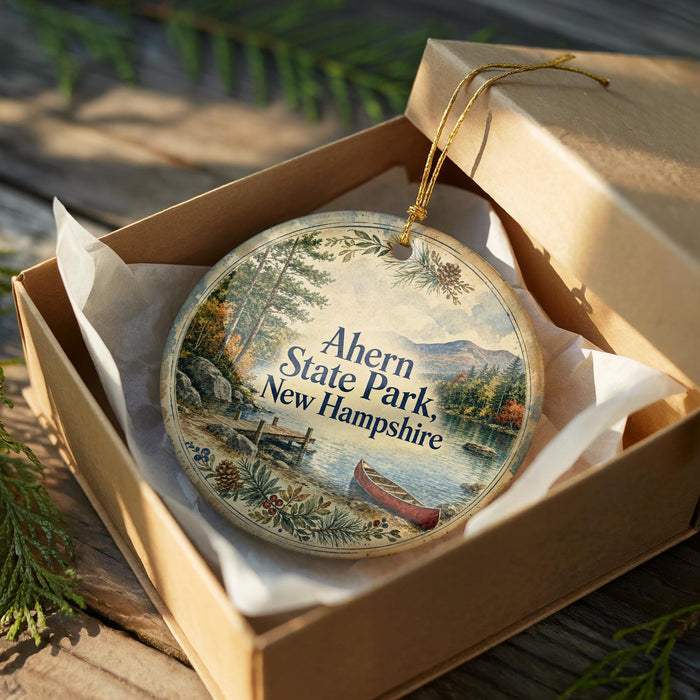 A decorative ornament in a wooden box, featuring a scenic landscape with a lake, mountains, and a canoe, with the text "Ahern State Park New Hampshire" printed on it.