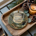 A decorative ornament featuring a scenic landscape of Ainsworth State Park, Oregon, with pine cones and a lit candle on a wooden tray.