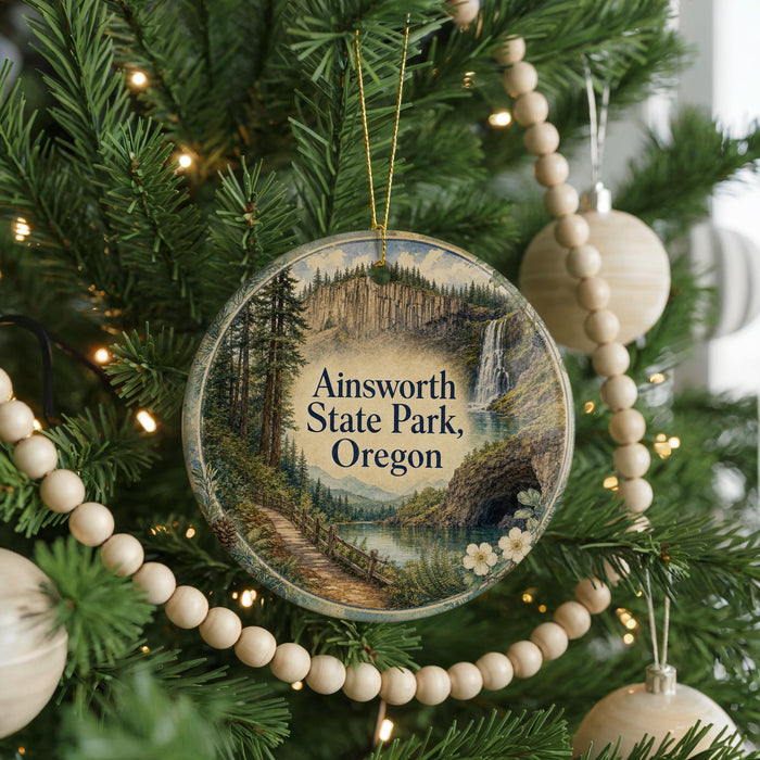 A round ornament hanging on a Christmas tree, featuring a scenic landscape with a waterfall and forest.