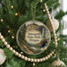 A round ornament hanging on a Christmas tree, featuring a scenic landscape with a waterfall and forest.
