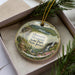 A decorative ornament in a box, featuring a scenic landscape with a waterfall and greenery.
