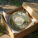 A decorative ornament in a box, featuring a scenic landscape with a waterfall and lush greenery.