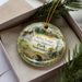 A decorative ornament in a box, featuring illustrations of a lodge, a house, a bridge, and a windmill, with the text "Arbor Lodge State Historical Park, Nebraska" printed on it.