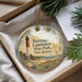 A decorative ornament with a lighthouse image and text, placed in a box with pine branches.