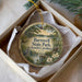 A decorative ornament in a box, featuring a scenic landscape with a pond, trees, and a bird.