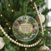 A round ornament hanging on a Christmas tree, featuring a scenic image of Bayard Cutting Arboretum in New York.